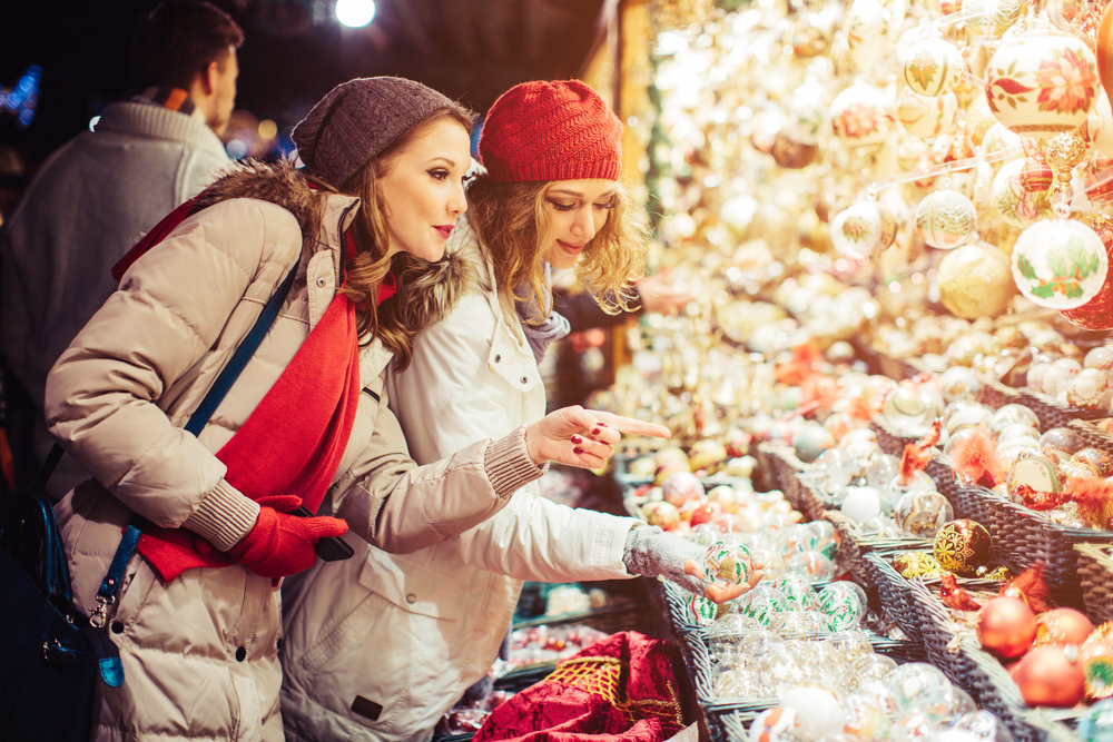 Friends shopping at christmas fair outdoors At Rathausplatz, Vienna, Austria. Wearing warm clothes, hats and scarfs. Looking at christmas decorations. Evening or night with beautiful yellow lights lightning the scenes.